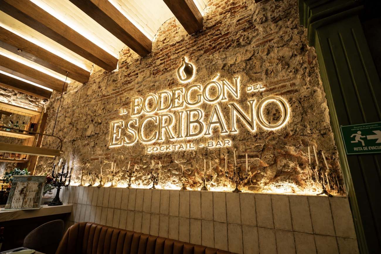 Muro de piedra con el letrero iluminado de El Bodegón del Escribano